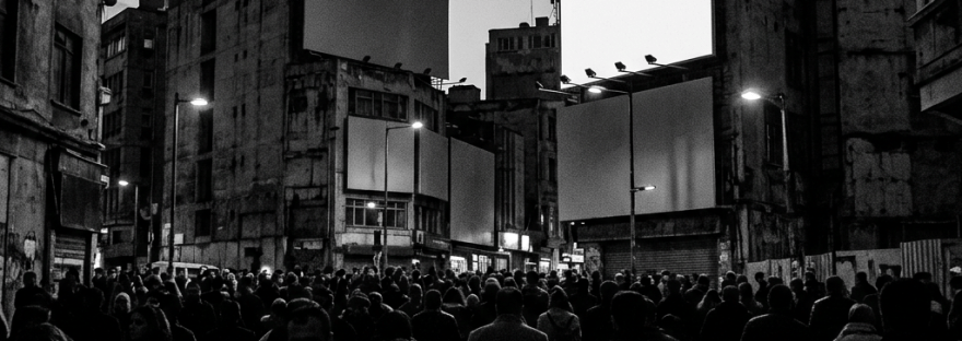 Crowd of people walking between buildings with large blank billboards overhead at dusk
